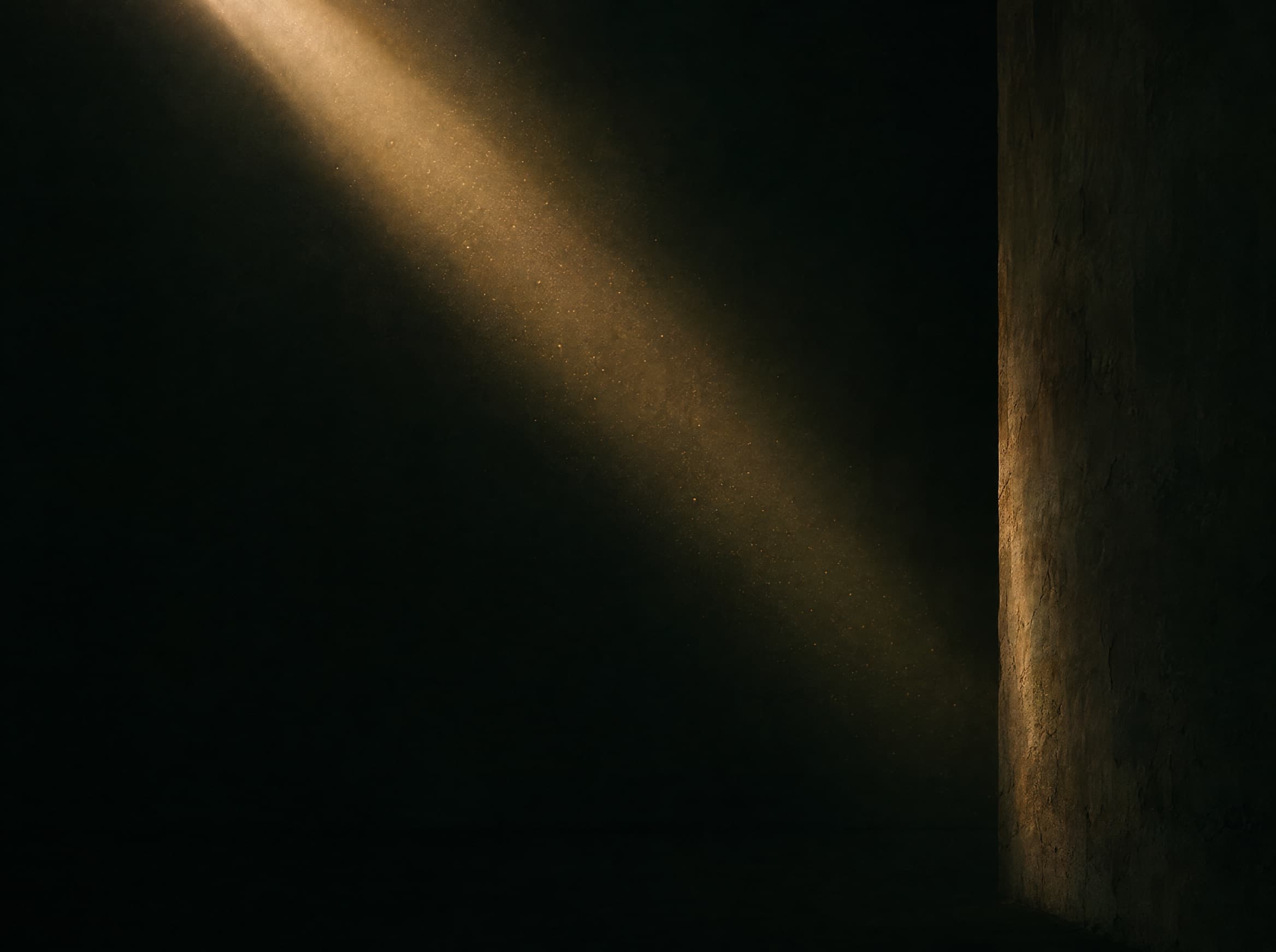 A single shaft of warm daylight entering a vast dark empty room.